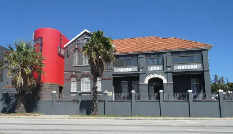 A gray double story building with white accents with a brown roof and a red portion to the left.